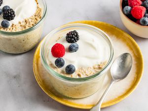 Two glass ramekins with overnight oats, topped with fresh berries, with a small bowl of berries in the background