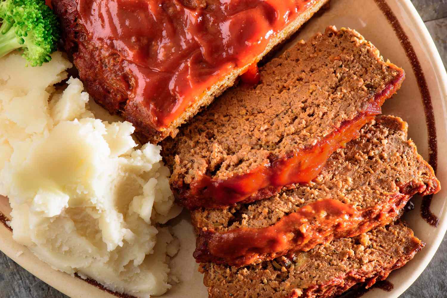 Closeup of meatloaf partly sliced on on a plate with a side of mashed potatoes