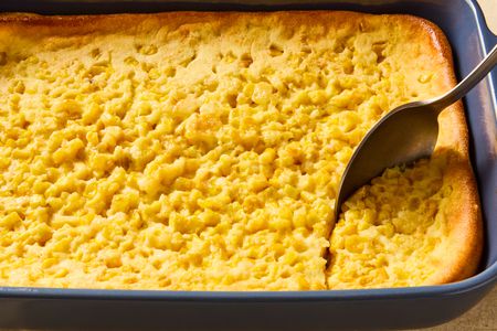 dark blue baking dish of corn soufflé with a spoon scooping out a serving