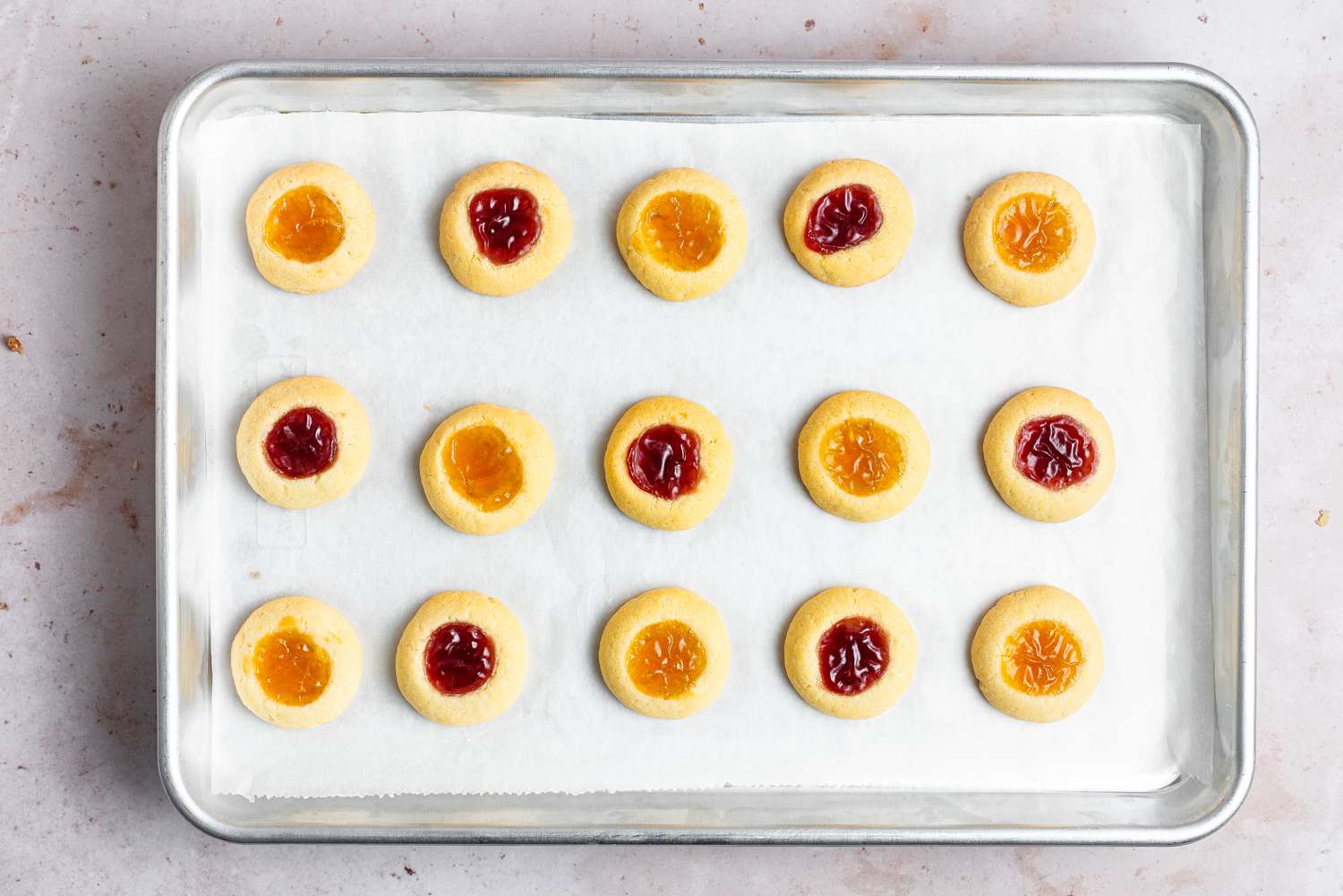 Baked thumbprint cookies on a baking sheet and filled with a variety of jams