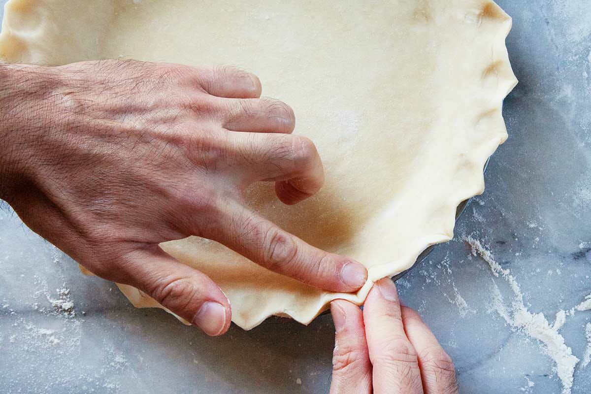 A pie crust is being crimped to show how to make a chess pie.