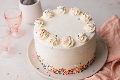 Decorated Rainbow Layer Cake on a Plate with Glasses in Background