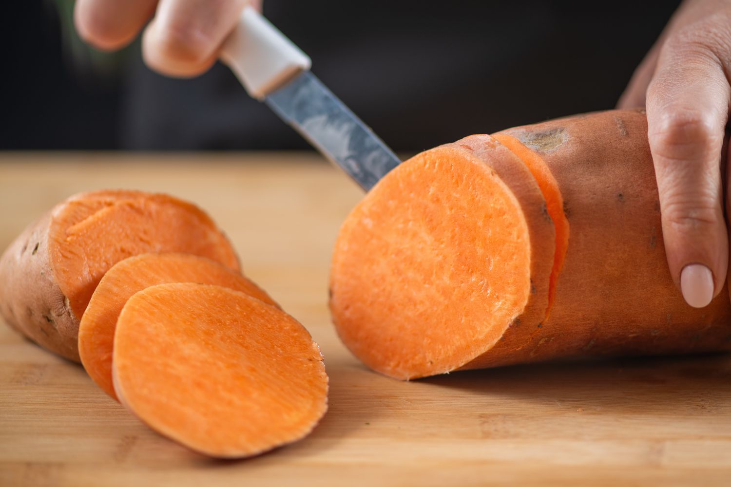 A sweet potato getting sliced on a wooden cutting board