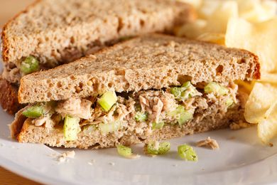 tuna salad sandwich (halved) on a plate with potato chips