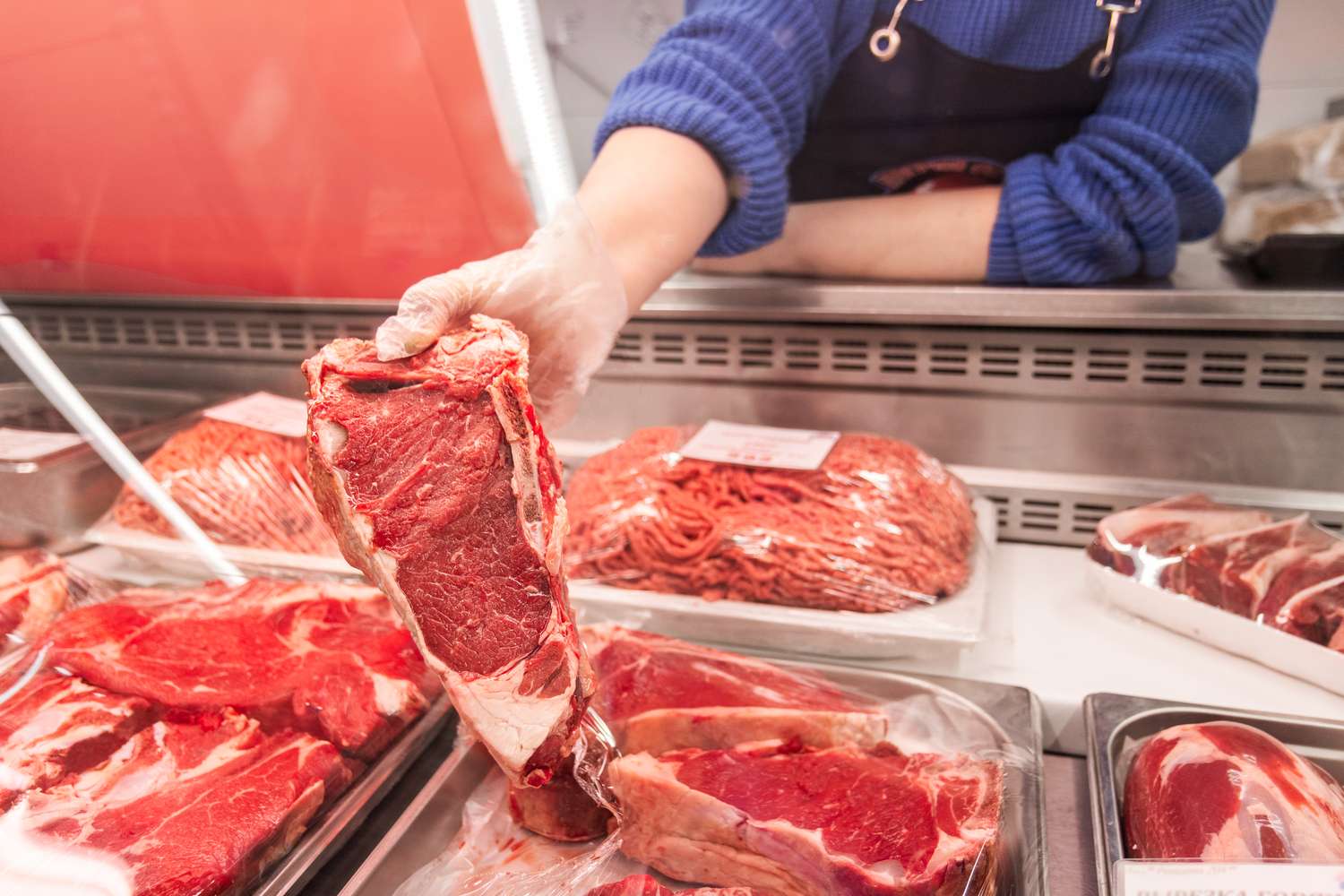 A hand holding a cut of raw meat in a butcher shop display