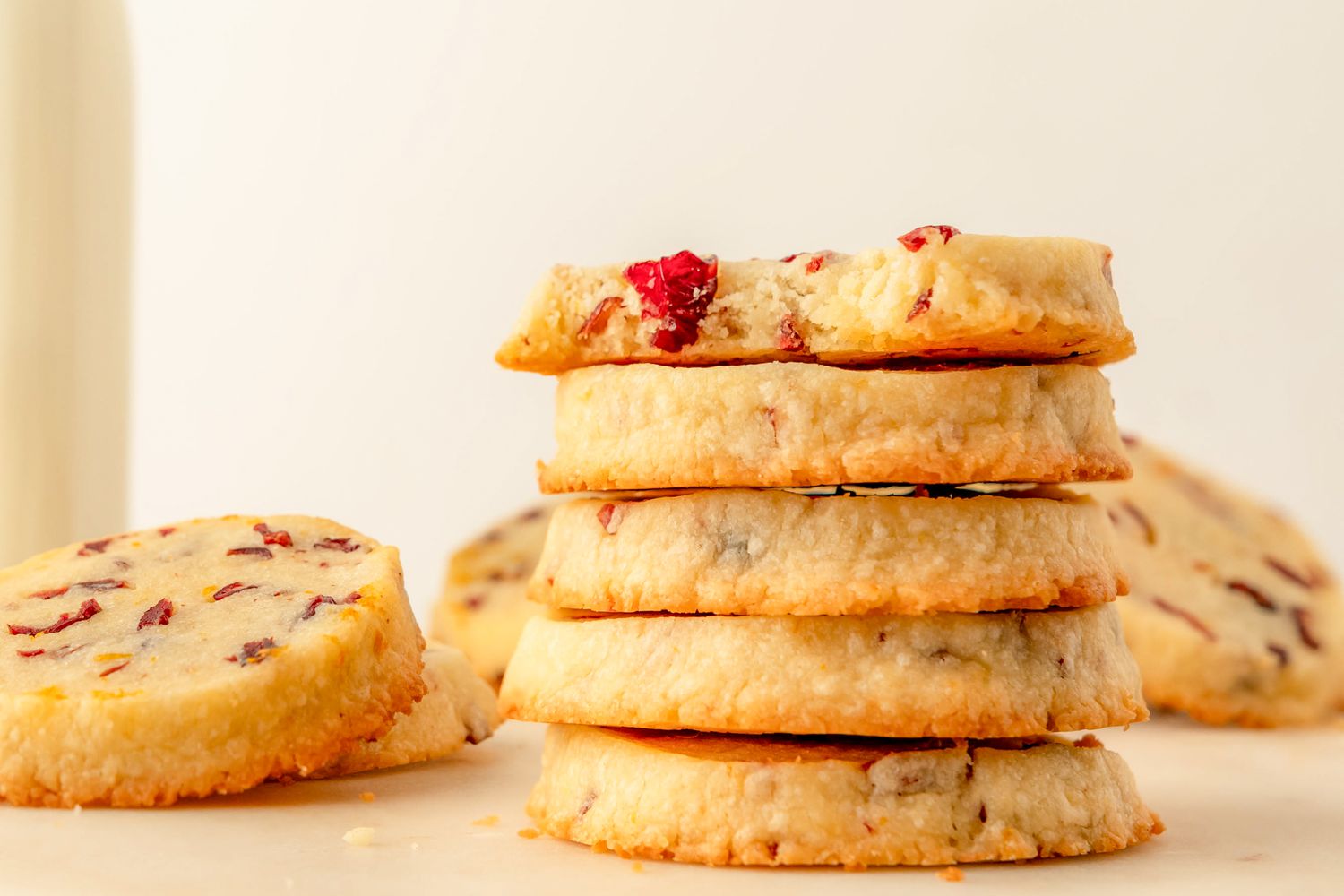 Side view of a stack of five cranberry orange shortbread cookies with more in the background