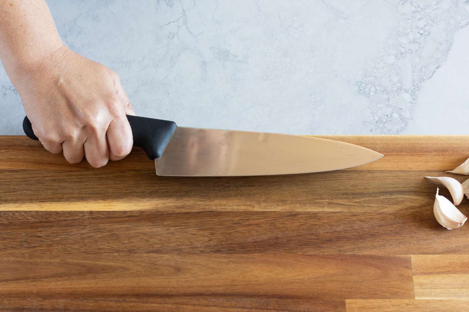 Chef's knife covering a garlic clove on a wood cutting board