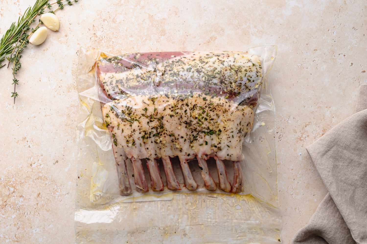 Method shot - Rack of lamb marinating in bag with garlic cloves rosemary and thyme on the side