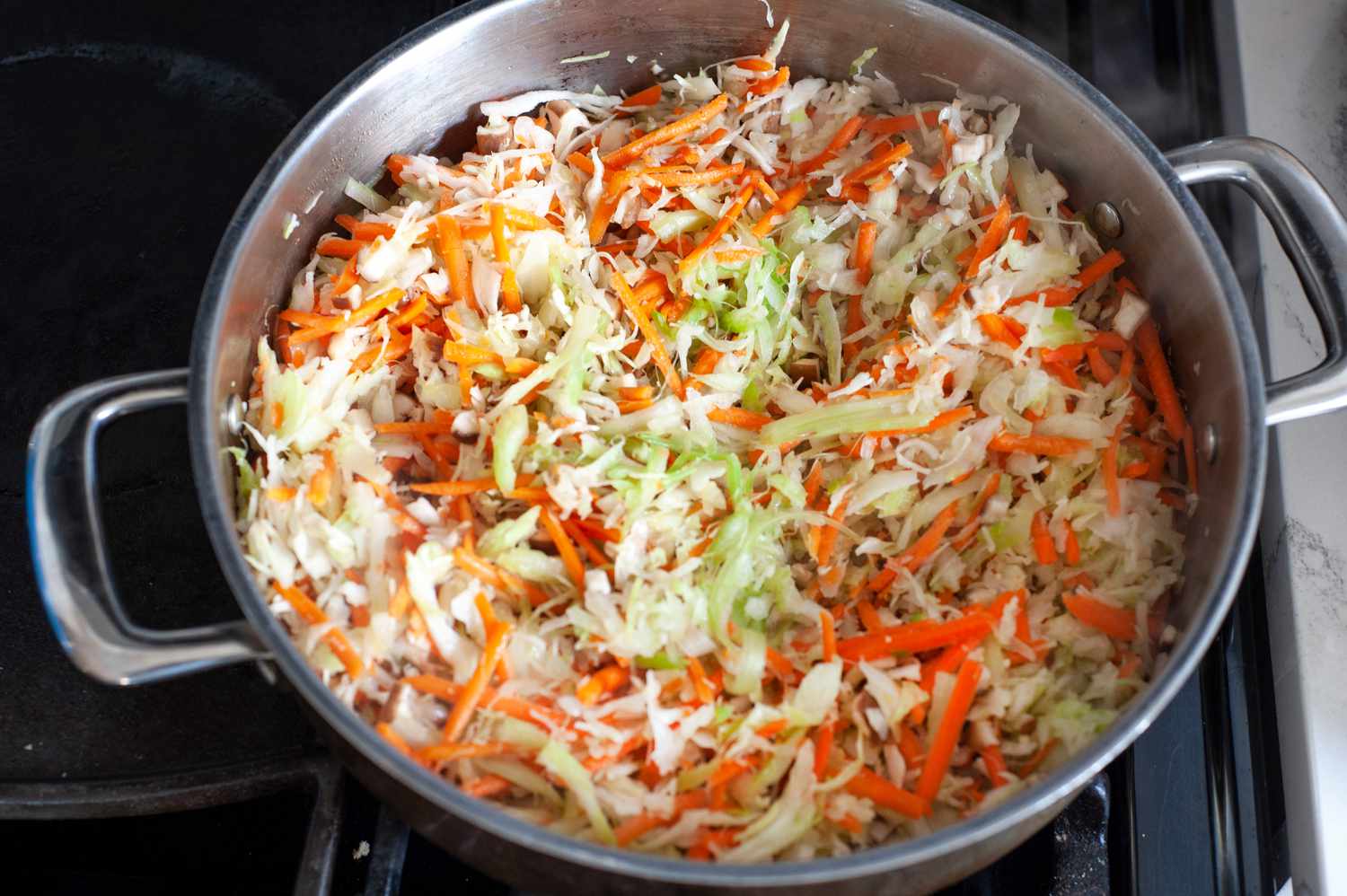Making the filling for fried egg rolls with cabbage, carrots, and mushrooms in a large pot.