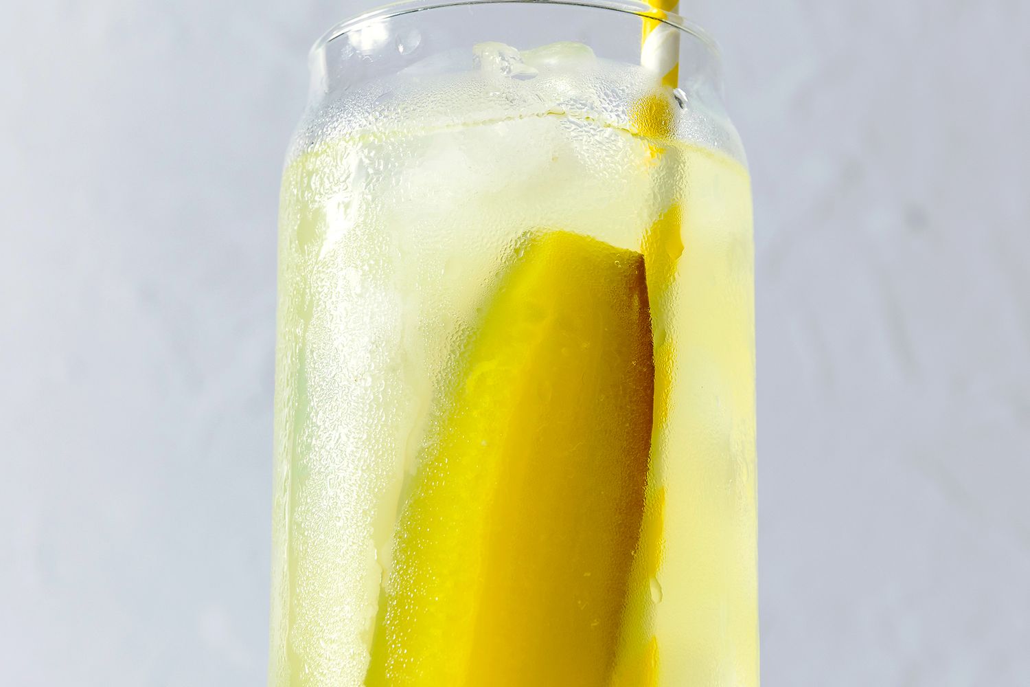 glass of iced lemonade with a pickle spear and a straw for Pickle Lemonade