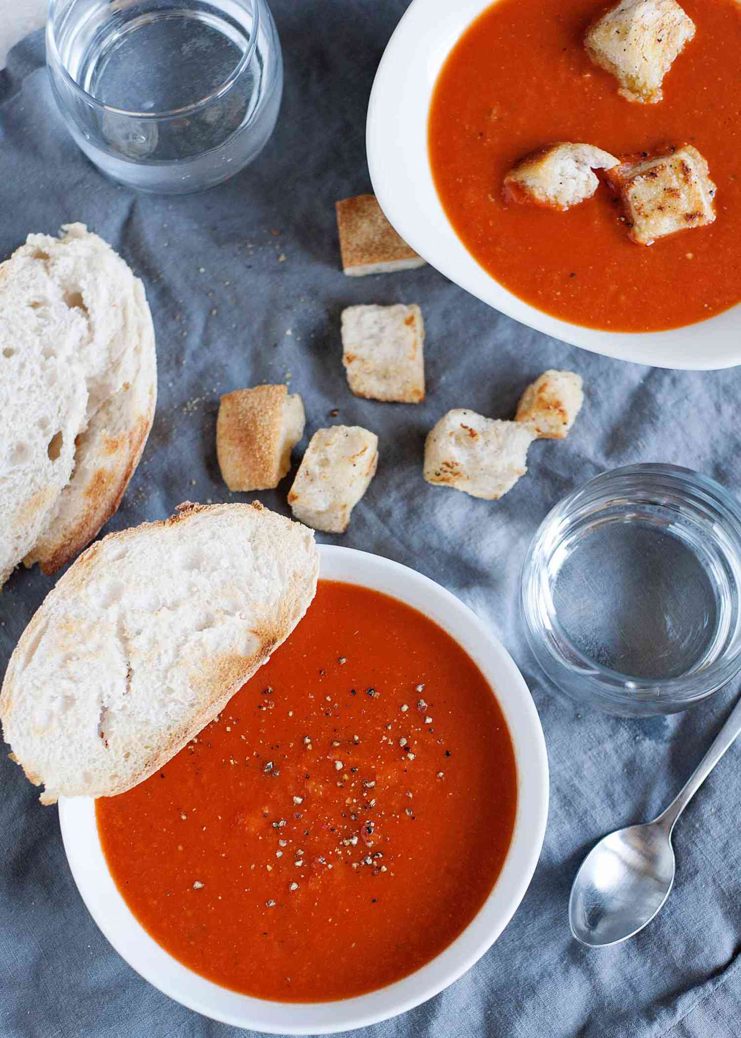 Easy Homemade Tomato Soup - tomato soup in a white bowl with a piece of bread, and pieces of bread crumbs on the table cloth