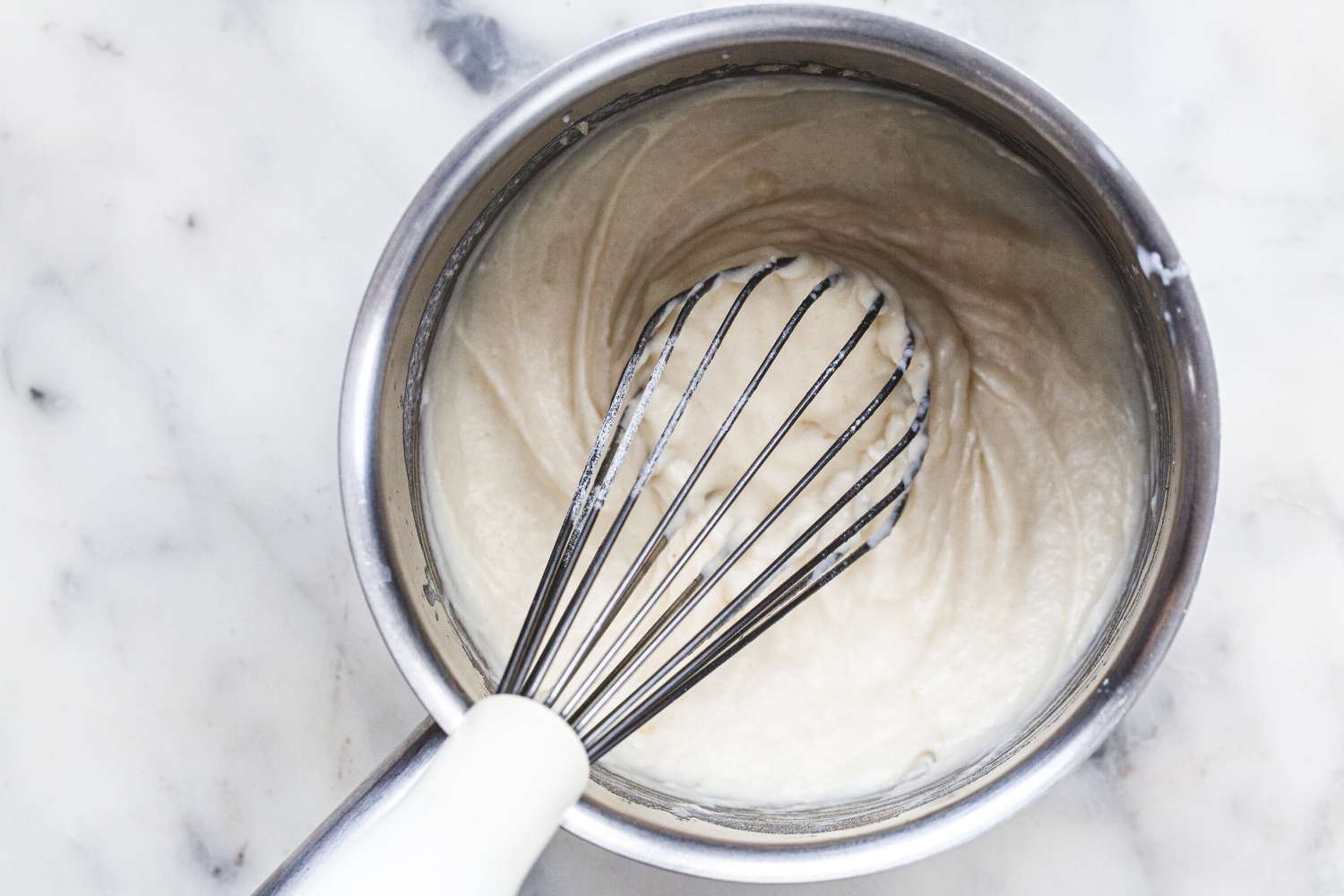 Whisking white sauce or béchamel sauce in a saucepan.