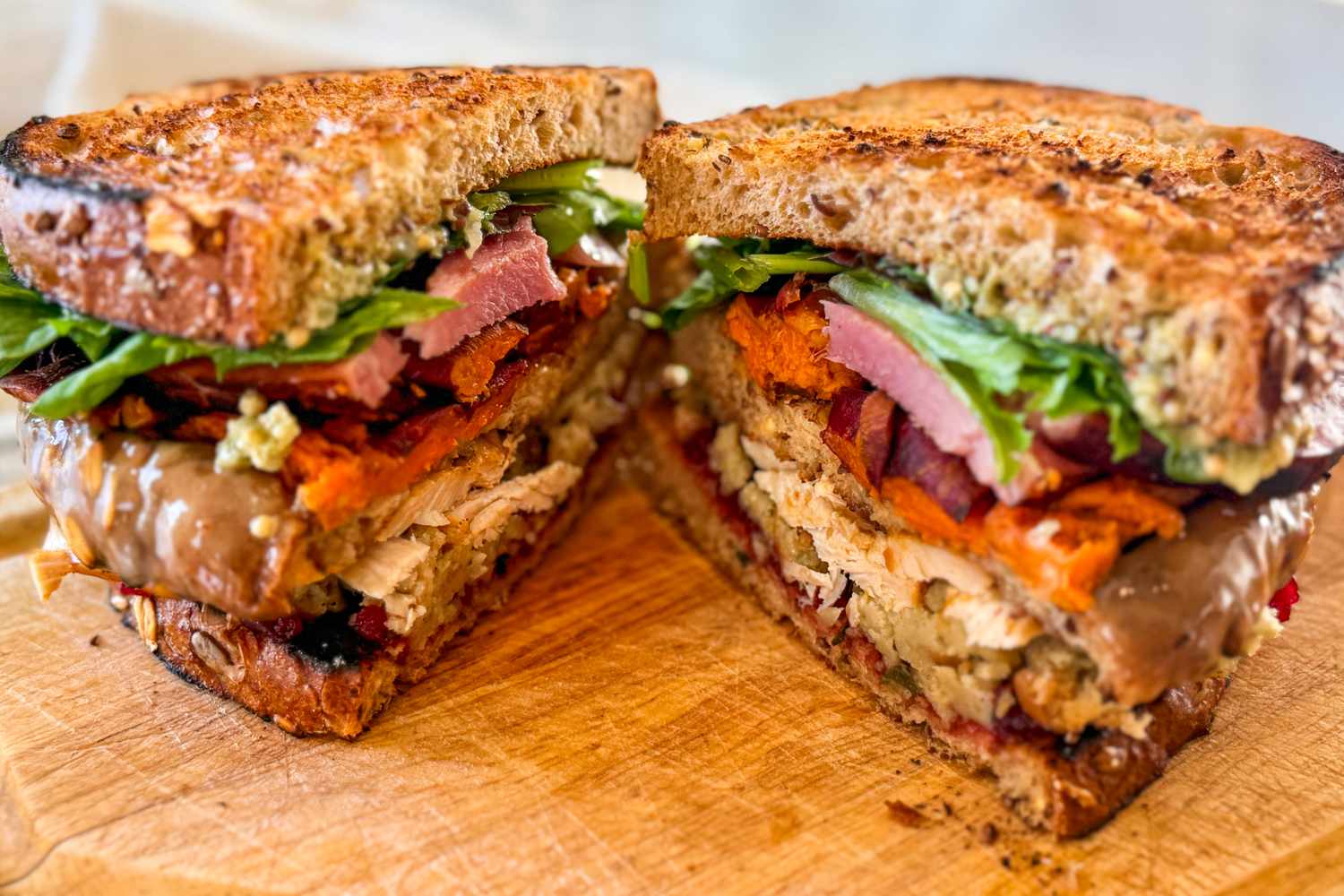 A layered sandwich cut in half revealing ingredients such as meat lettuce and sauce on toasted bread