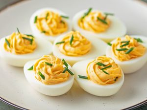 Deviled eggs topped with chopped chives served on a white plate
