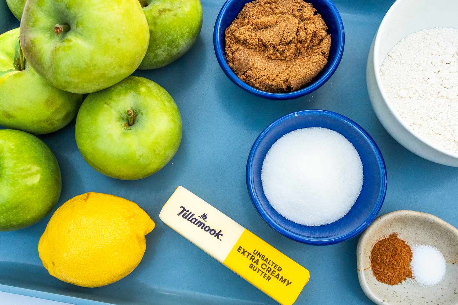 Ingredients for an apple recipe including green apples lemon butter brown sugar white sugar flour and spices