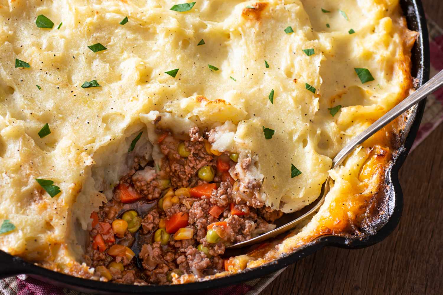 Shepherds pie in a cast iron skillet with a serving spoon showing the layers of mashed potatoes and meat filling