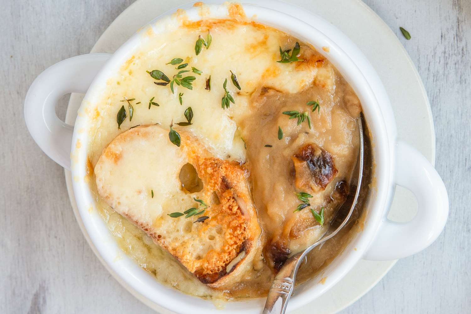 A bowl of French onion potato soup topped with melted cheese and herbs with a spoon inserted