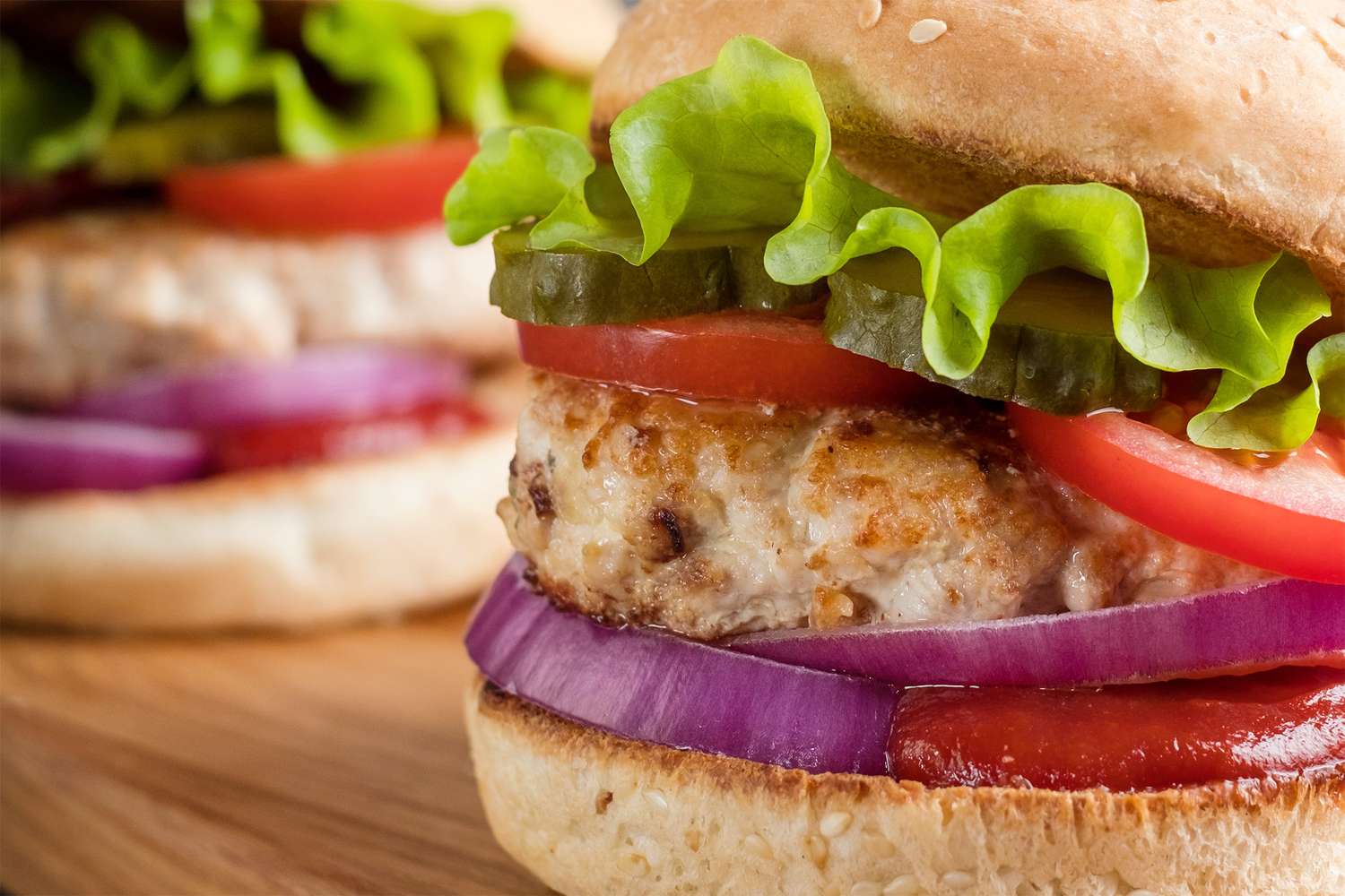 Close-up view of turkey burgers in buns with lettuce, tomato, red onion, and pickles