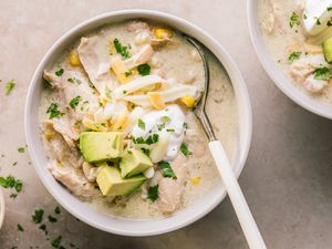 A bowl of chicken enchilada soup garnished with avocado sour cream and shredded cheese with a spoon placed in the bowl
