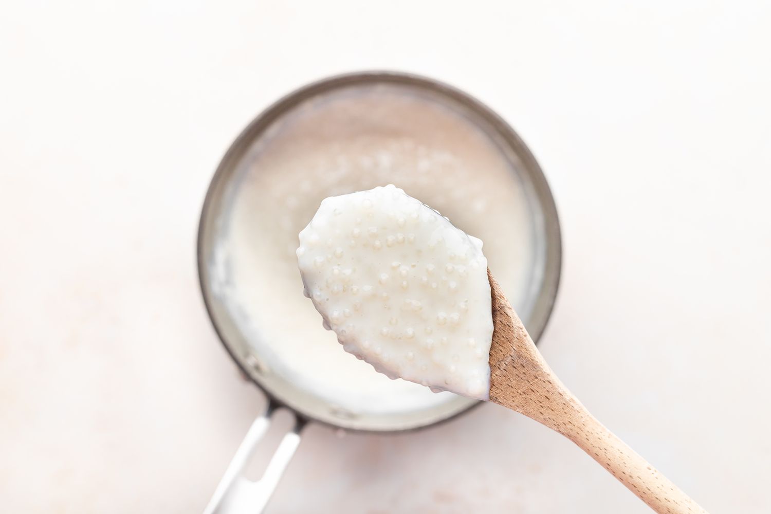 A wooden spoon with tapioca pudding scooped out of a pot.