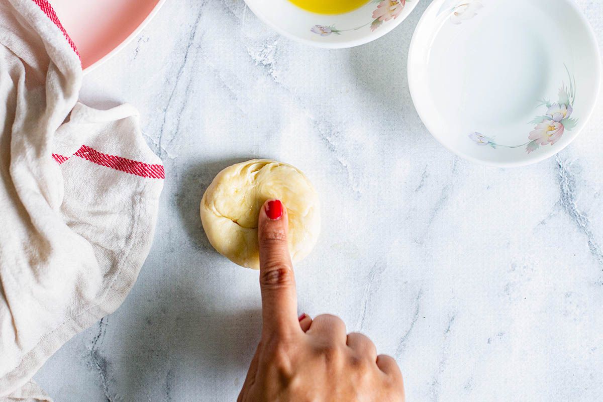 Womans finger with red nail pressing on a dough round.