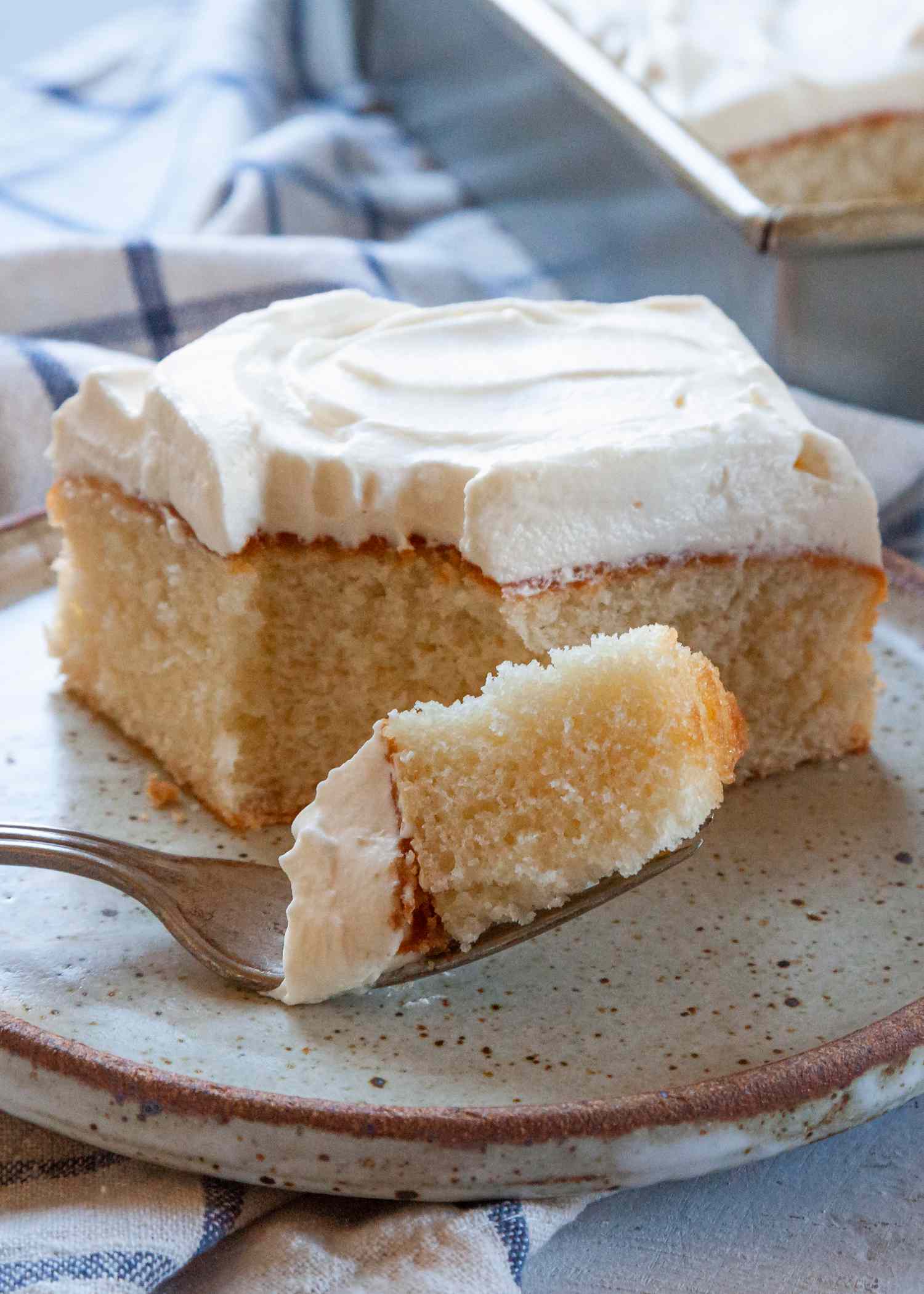 Side view of a copycat box white cake topped with frosting and on a plate with a bite on a fork.