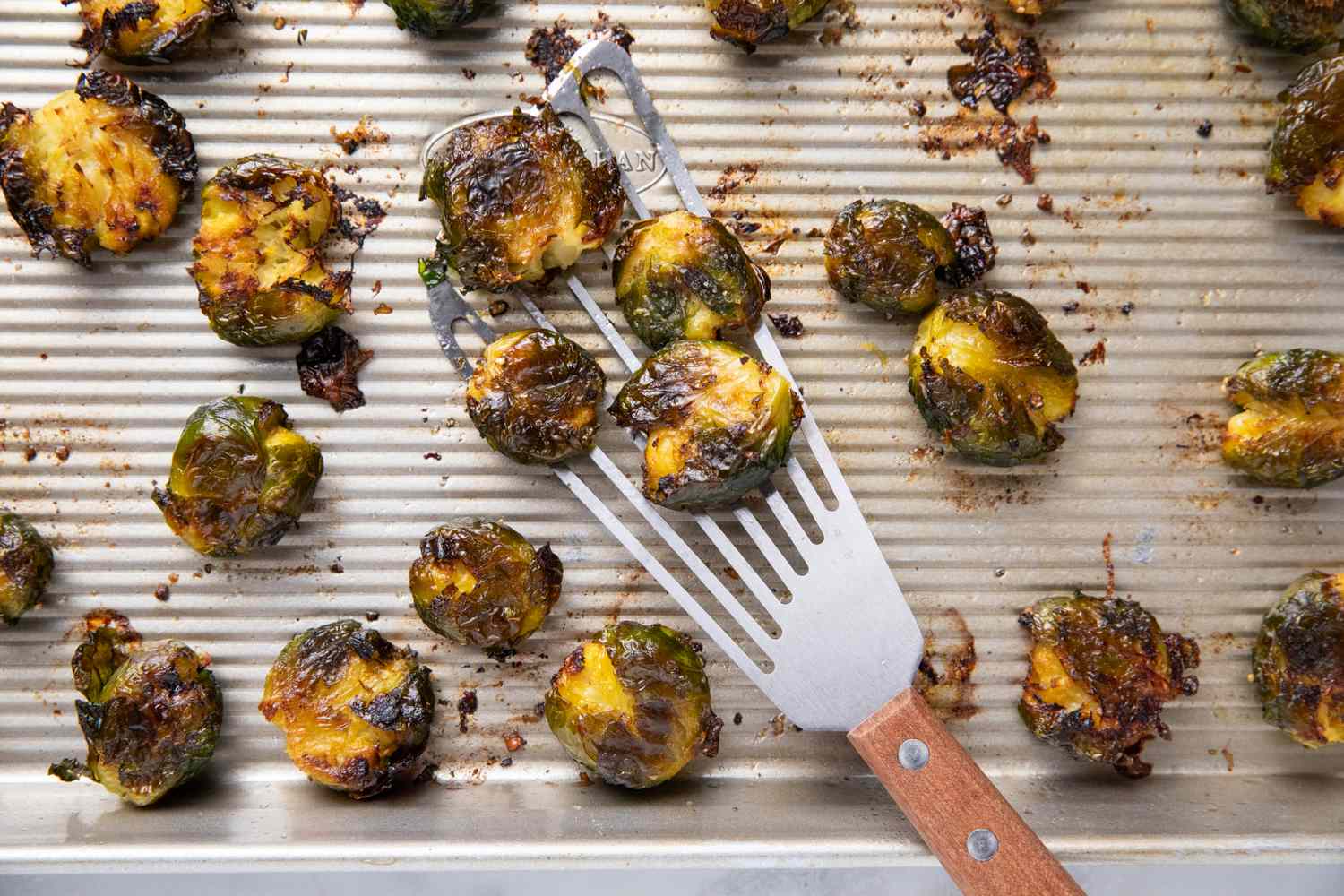 Sheet pan with cooked smashed Brussels sprouts and a spatula