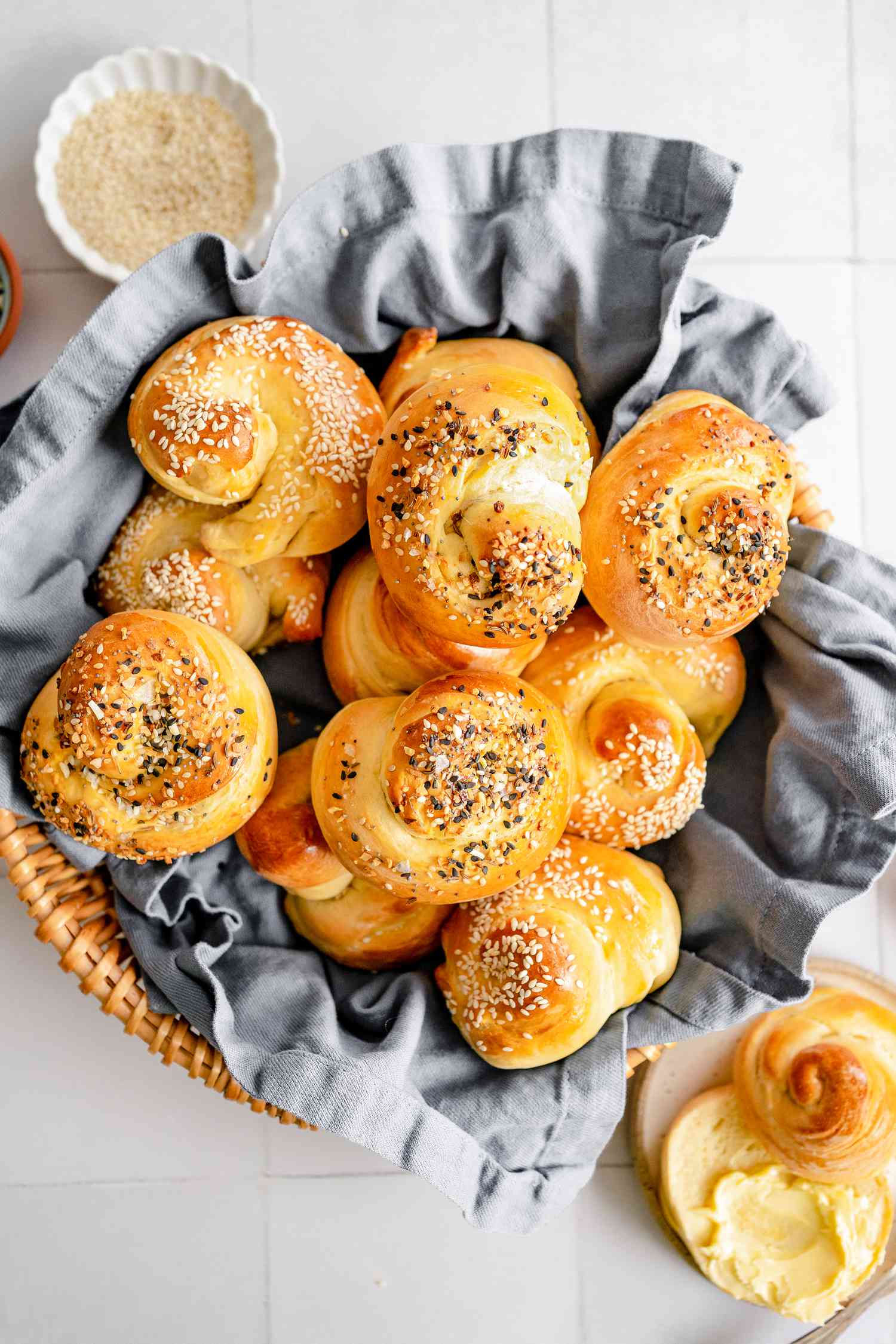 Basketful of Challah Rolls Next to One Cut in Half and Smeared with Butter