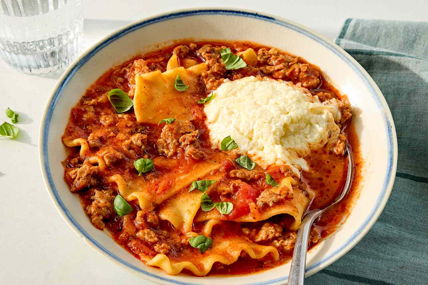 A bowl of lasagna soup topped with ricotta cheese and basil