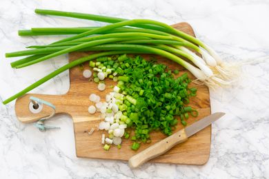 Overhead shot of a bunch of scallions, part of them chopped up, on a wooden cutting board