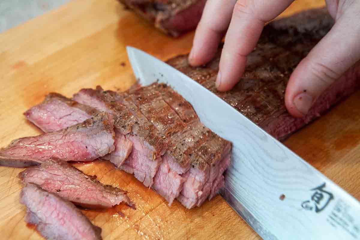 grilled flank steak being cut into slices with knife