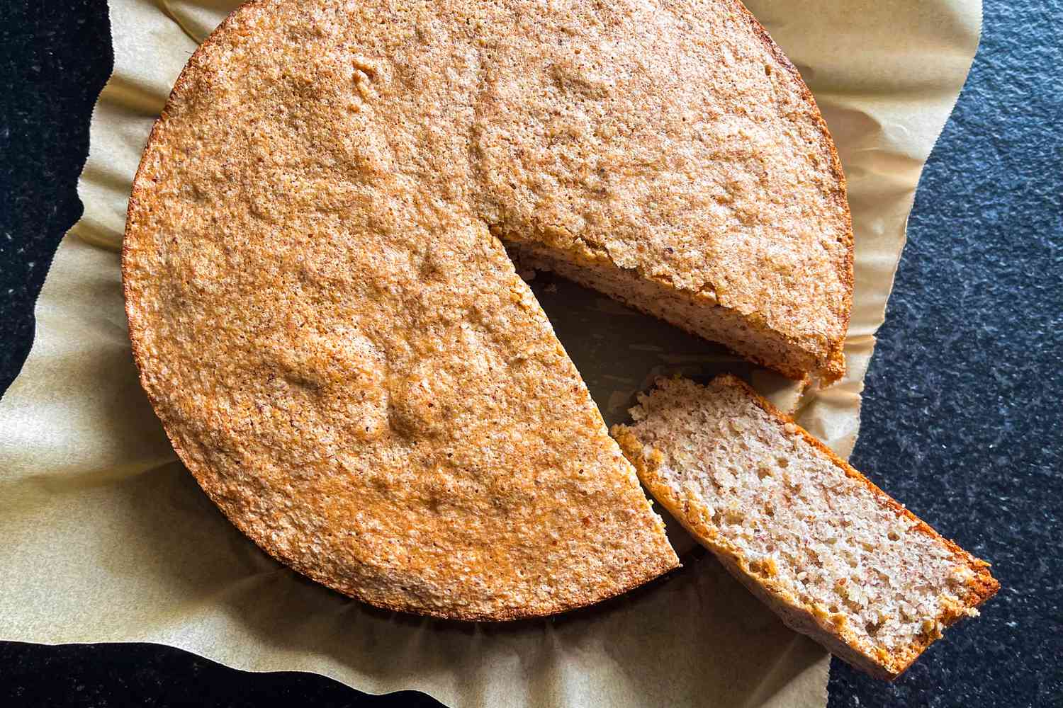 A round almond cake on parchment paper with a slice cut and separated slightly