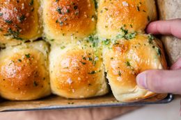 A hand grabbing a pull apart rolls with garlic and parmesan out of a pan.