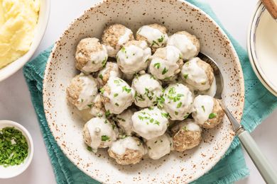 A bowl of meatballs covered in a creamy sauce garnished with parsley
