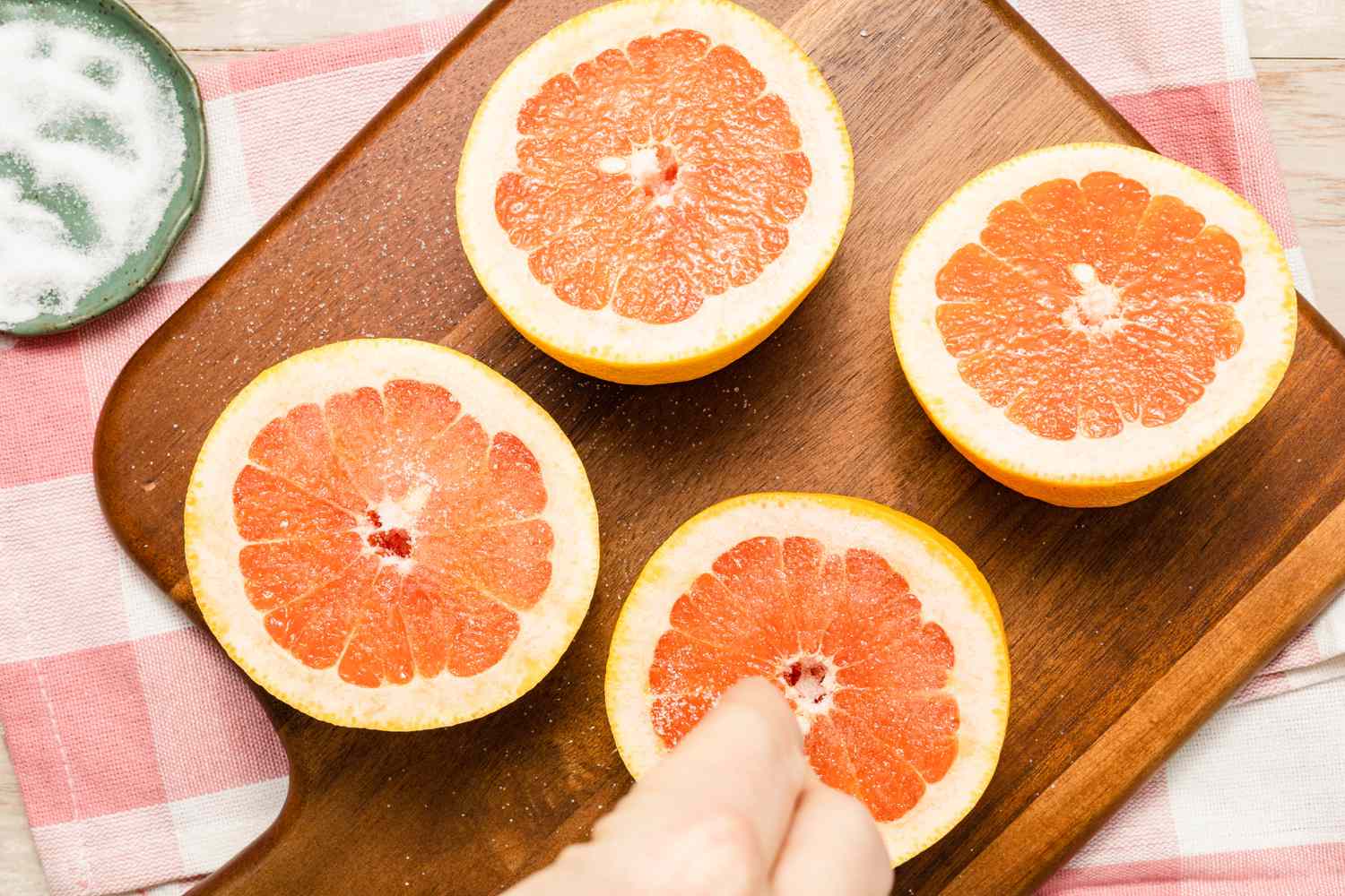 Sugar Pinched Onto Halved Grapefruit on a Wooden Cutting Board Next to a Small Saucer With More Sugar for Grilled Grapefruit Paloma