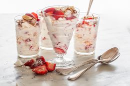 Glasses and Parfait Cups of Strawberry Eton Mess with Some Strawberries and Spoons on the Counter