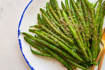 A plate of green beans garnished with a seasoning or sauce, arranged neatly with a bright and clean presentation