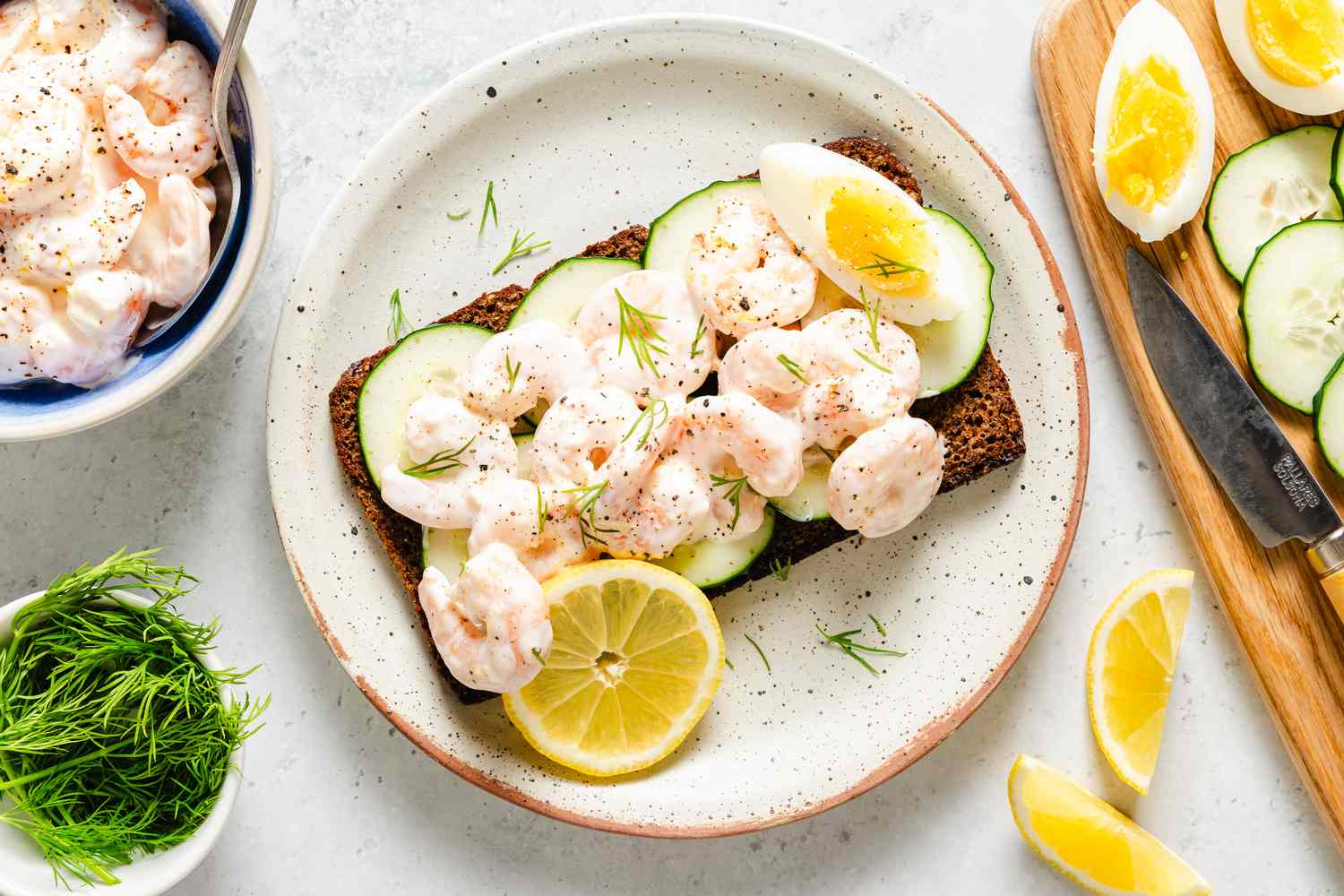 Scandinavian Shrimp Sandwich on a plate, garnished with wedge of a boiled egg, chopped fresh dill, and a lemon slice