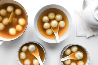 Three Bowls of Red Bean Tangyuan with Soup Spoons, and on the Left, a Pot with More and on the Right, a Tea Kettle Sitting on Napkins