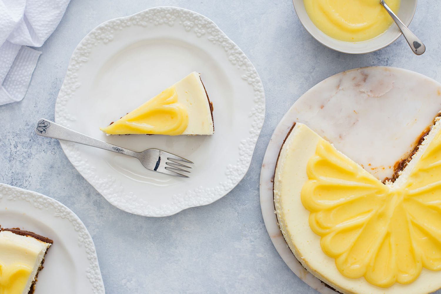 Lemon cheesecake slice on a plate with a fork next to the cut cheesecake