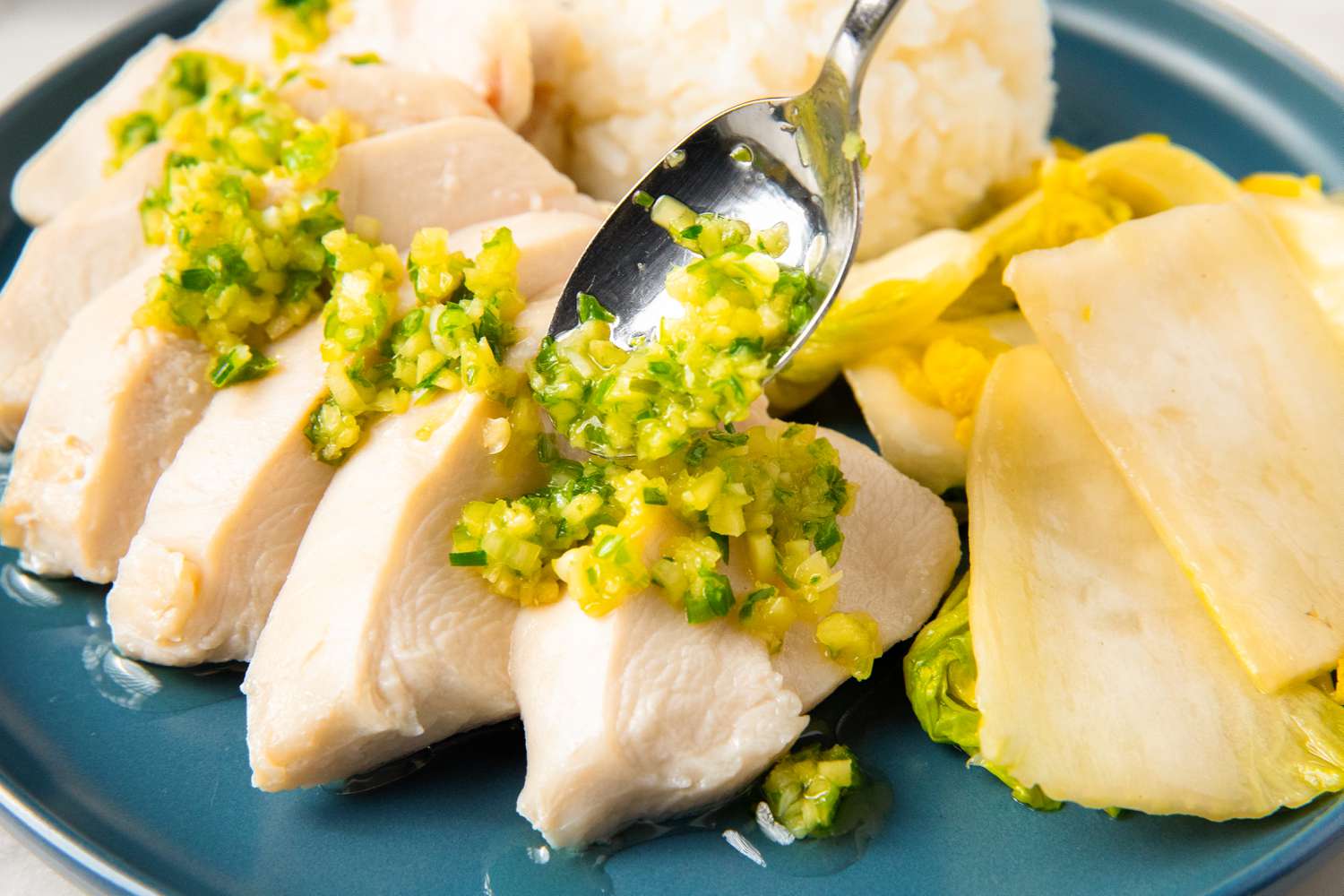 A plate of sliced chicken topped with a scallion sauce, served with rice and pickled vegetables