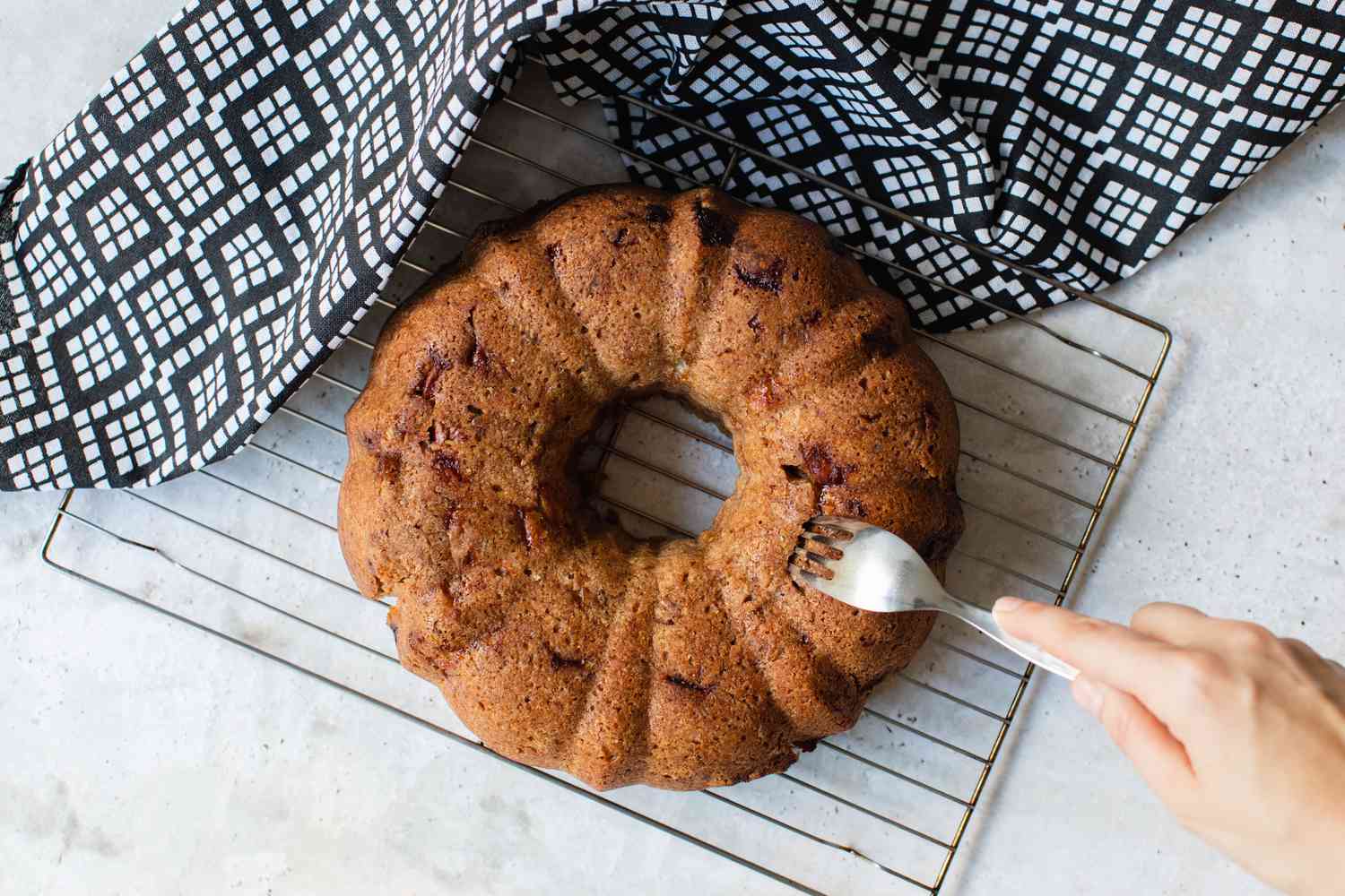 Fork Used to Poke Holes into Fresh Apple Bundt Cake Sitting on Cooling Rack