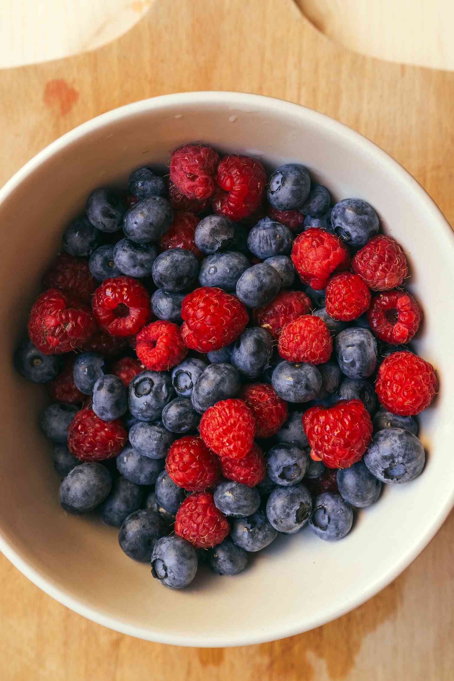Blueberry and raspberry mix in white ceramic bowl on wooden table