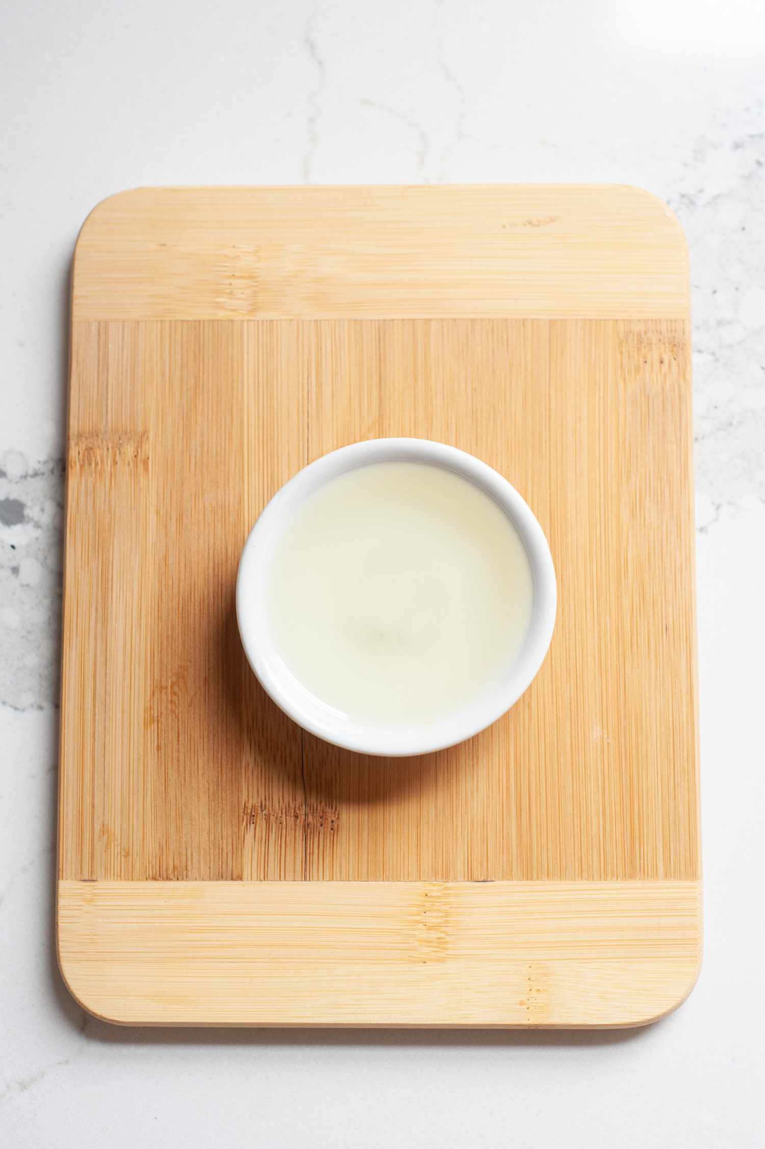 Walnut oil in white dish on wood cutting board