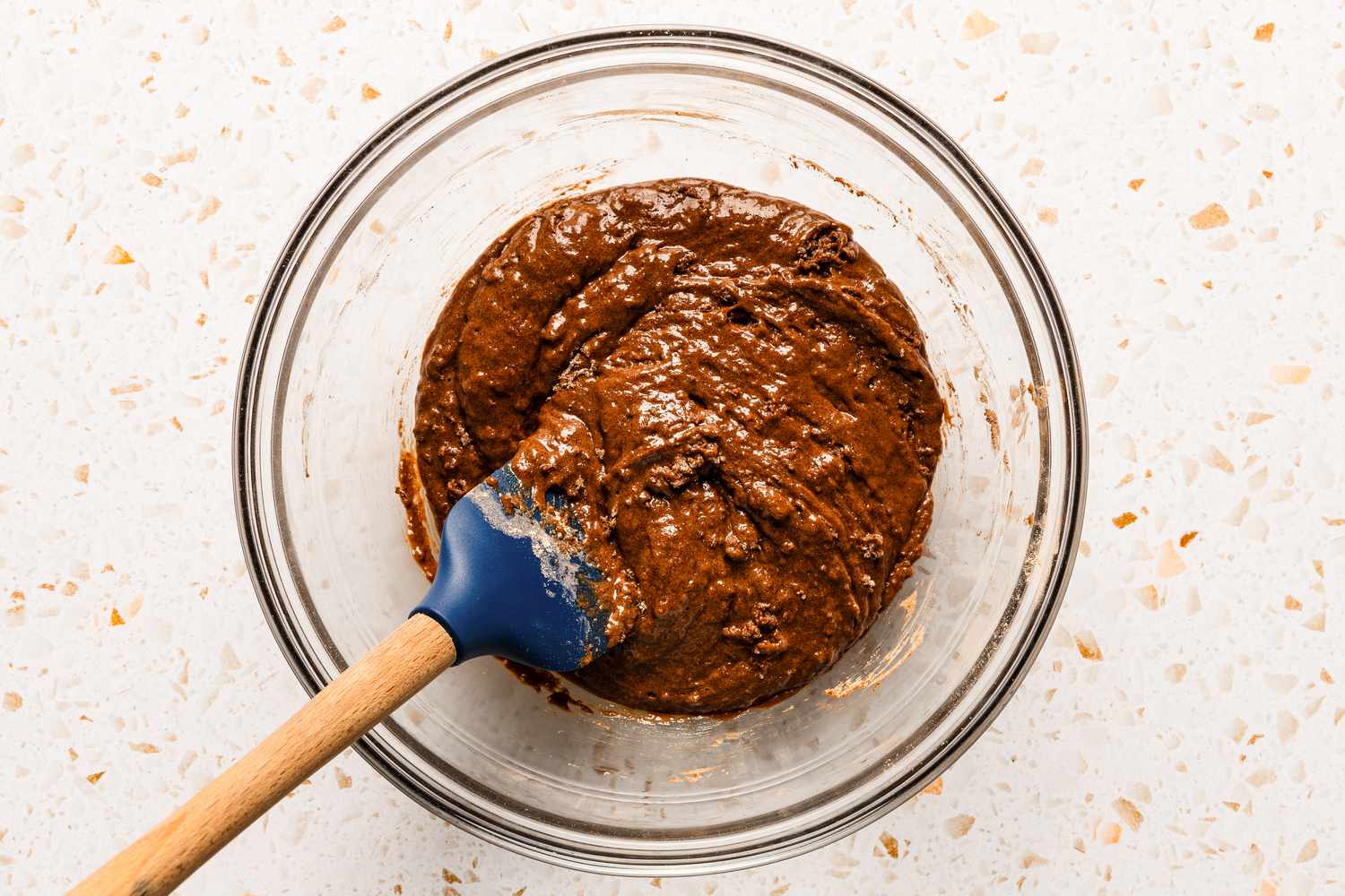 Batter being mixed with a spatula in a clear mixing bowl for chocolate cobbler recipe