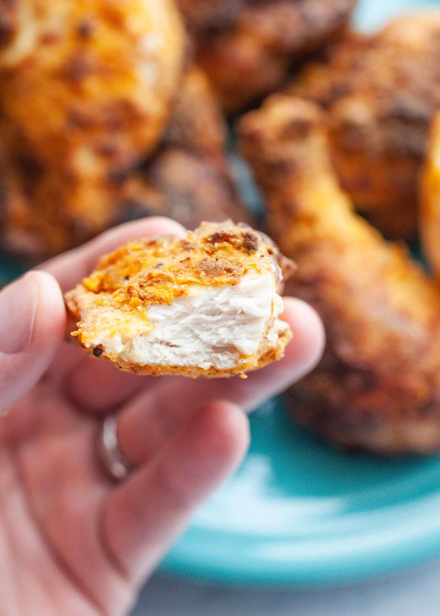 A hand holding a bitten into piece of air fryer fried chicken