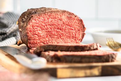 A partially sliced roast beef on a wooden cutting board