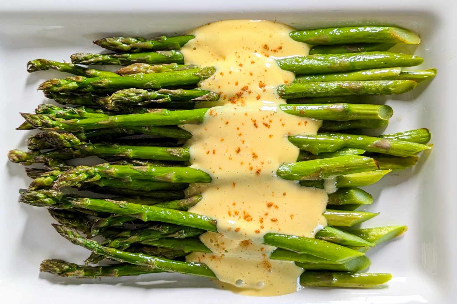 Overhead view of a white plate of roasted asparagus with Hollandaise sauce