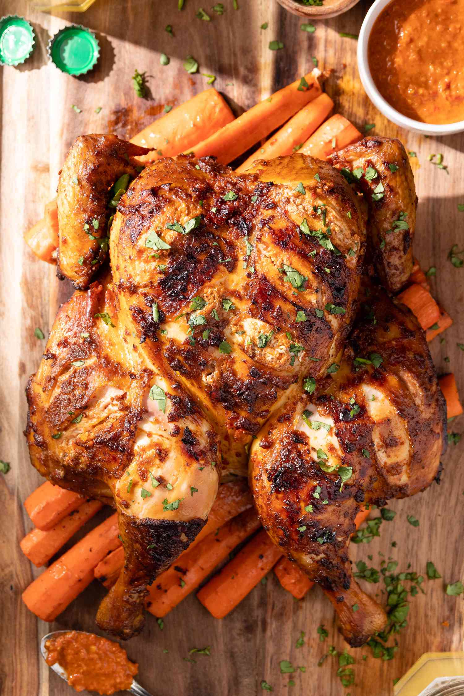 Smoked Spatchcock Chicken with Harissa Butter and Grilled Carrots on Cutting Board, Surrounded by Bowl of Harissa and Spoon