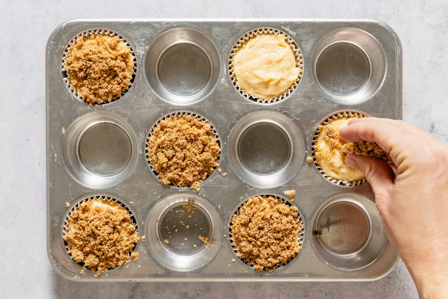 Hand adding crumb topping to muffin batter in a muffin pan
